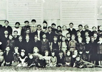 Schoolchildren and their teachers posed in rows before a white building.