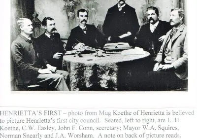 Men in suits posed around a table, with a printed caption below identifying Henrietta’s first city council.