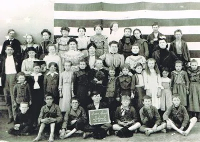 Dozens of schoolchildren in rows outside a frame school.