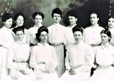 Young women in white dresses and a few young men posed in rows.