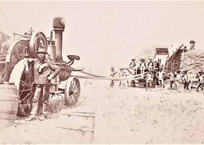A steam-powered threshing outfit stands in a stubble field with its crew posed beside the machinery.