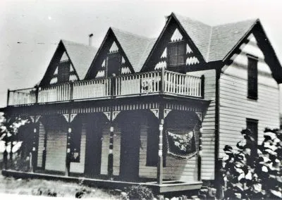 A Victorian frame house with gingerbread trim, a family posed on the porch.