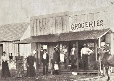 A wooden storefront with a “Groceries” sign, people posed in front.