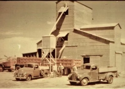A tall wooden grain elevator with trucks parked beside it.