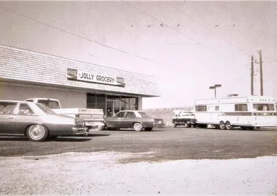 A small-town grocery storefront with a car parked at the curb.