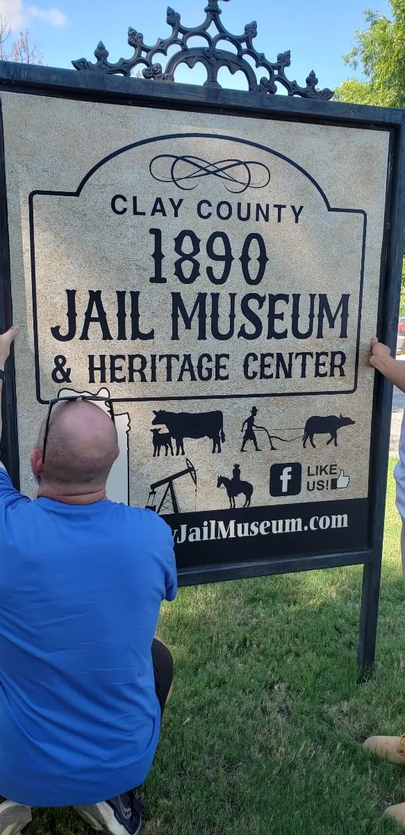 Two volunteers in blue shirts guide the new sign panel into the iron frame.