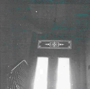 A dim interior view looking up toward a bright doorway crowned by a decorative transom, with a stair rail in the foreground.