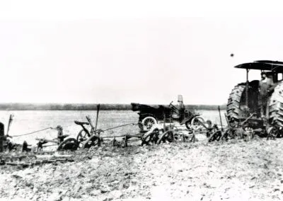 An early tractor pulls a gang of four disc plows across an open field.